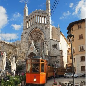 Orange vintage tram in front of the church with a rose window in the main square of Sóller