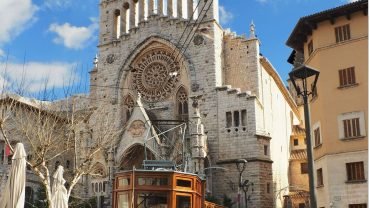 Orange vintage tram in front of the church with a rose window in the main square of Sóller